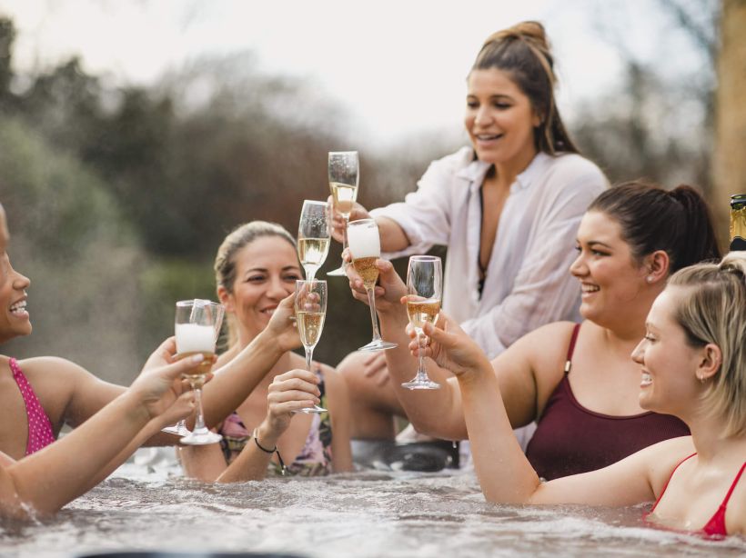Five girls in a hot tub holding up wine glasses to cheers each other at Spring Creek Vacations