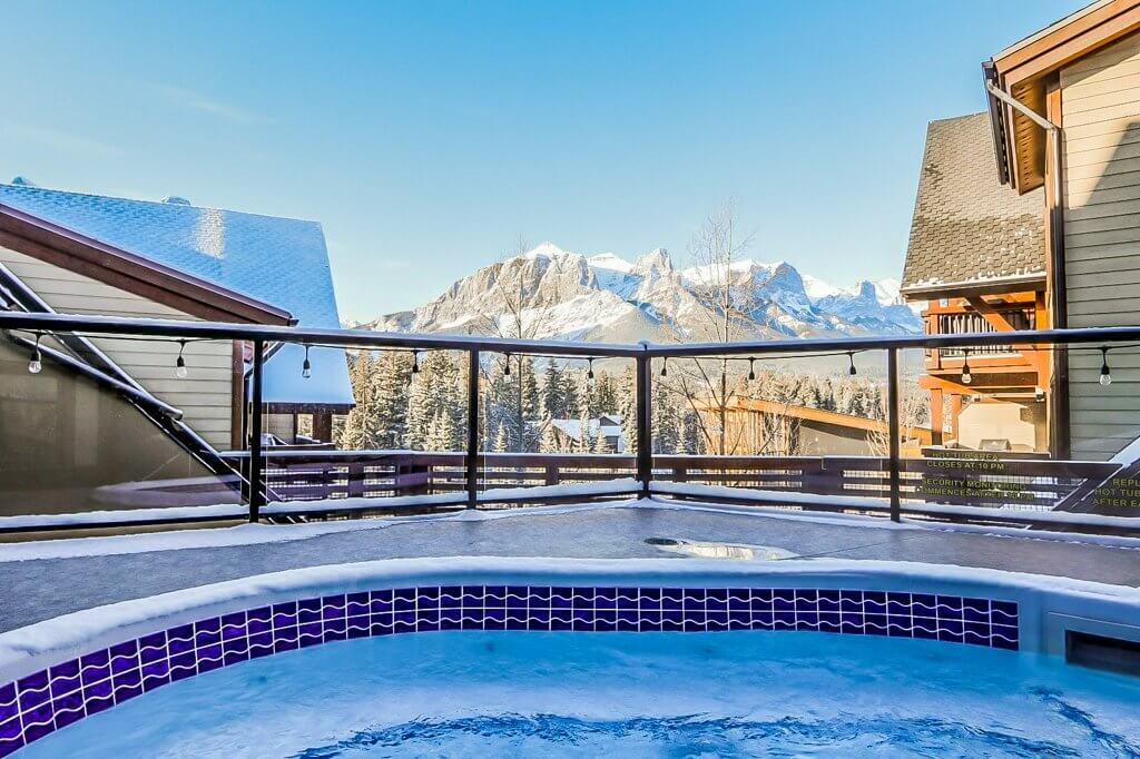 Mountain view of Canmore from the perspective of the hot tub at Spring Creek Vacations, during a bright blue skied day.