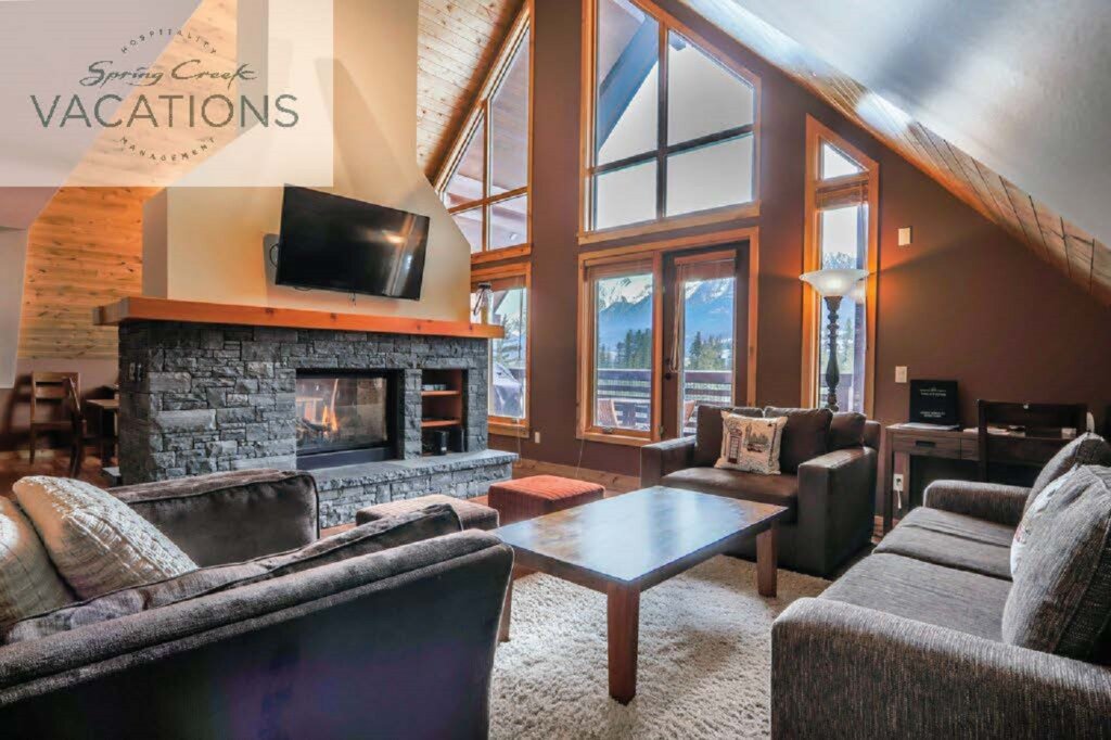 A large but cozy living room with a fireplace, floor to ceiling windows and relaxing, modern furniture in a luxury suite at Rundle Cliffs Lodge at Spring Creek Vacations in Canmore, Alberta