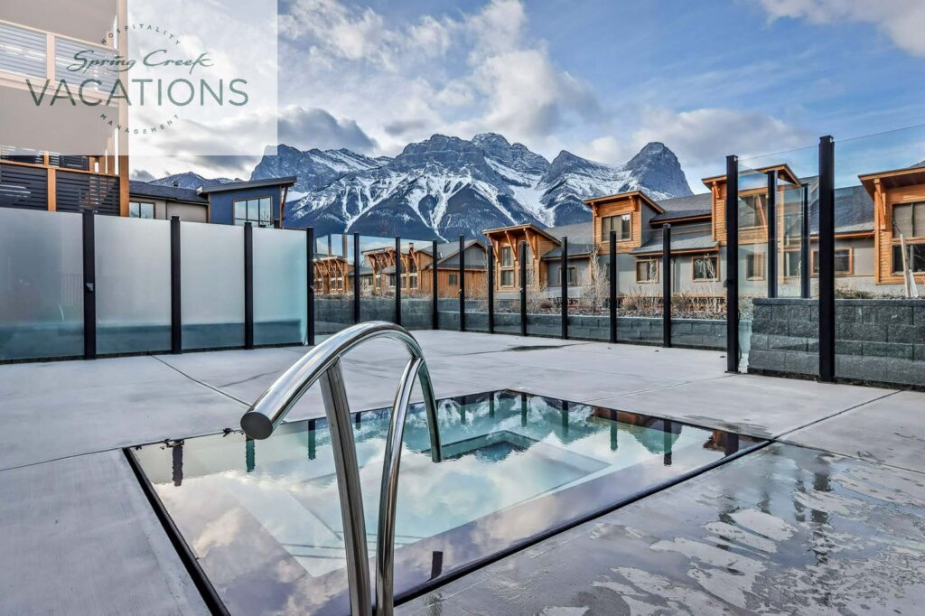 A hot tub with still, reflective water on a rooftop facing the Canmore mountains at Spring Creek Vacations luxury vacation rental White Spruce Lodge