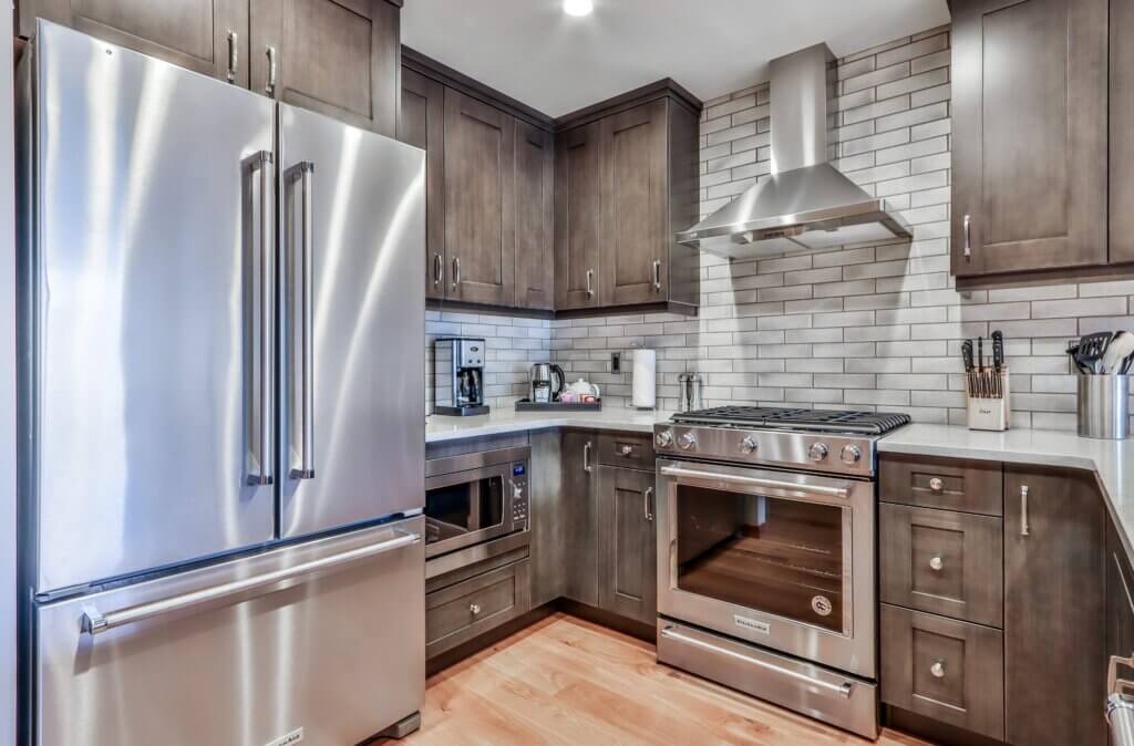 A corner of a luxury modern kitchen with a stainless steel double-door fridge, dark cabinets, grey tile backsplash and modern appliances in a Spring Creek Vacations suite in Canmore, Alberta