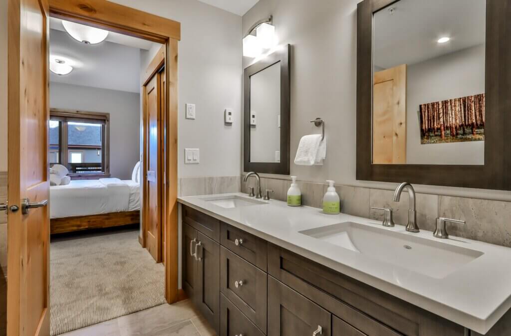 A luxurious bathroom. with white countertops and dark cupboards and modern accents in a Spring Creek Vacations suite in Canmore, Alberta.