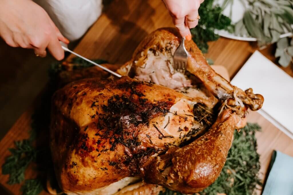 A herb-roasted turkey on a counter with a person standing over the turkey, carving a leg