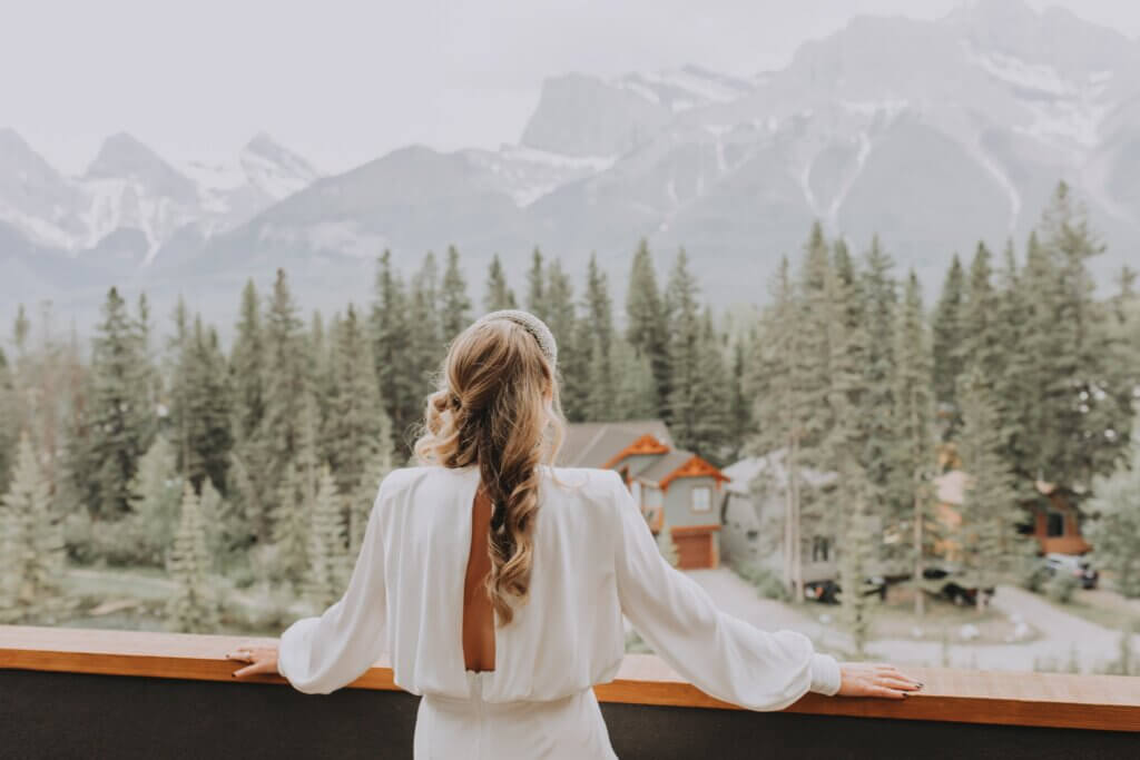 The back of a bride standing on a balcony overlooking the mountain range in Canmore in the Spring Creek neighbourhood.