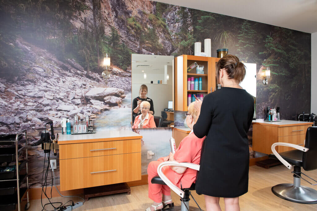 A hairstylist styles a senior's woman's hair at the Evergreen Spa and Salon at Origin at Spring Creek, one of Spring Creek Vacations' neighbours in Canmore.