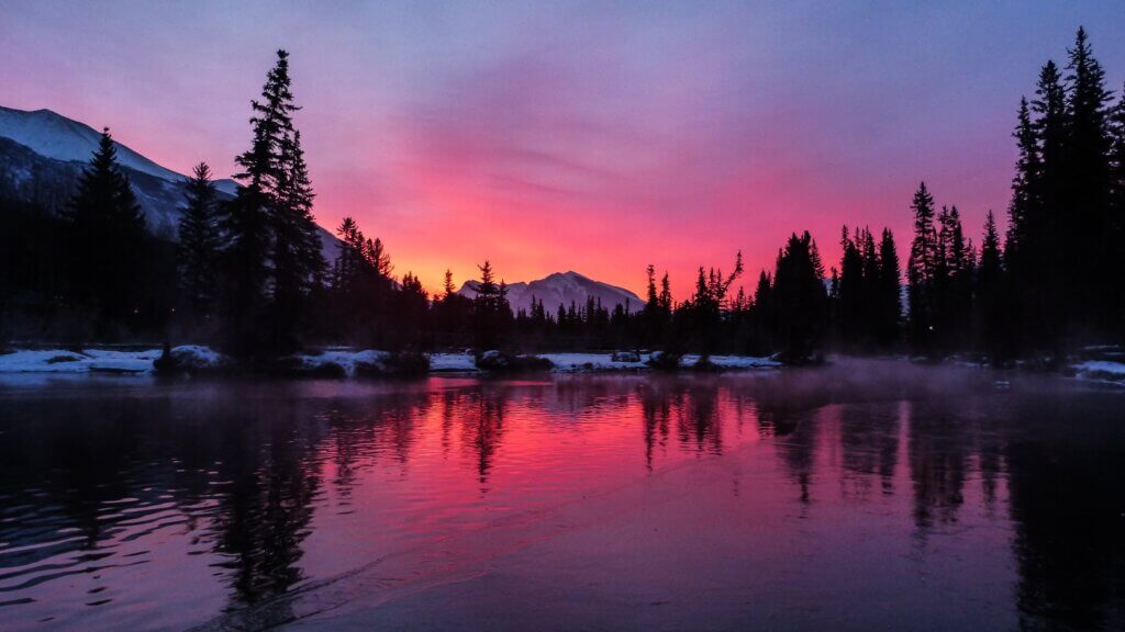 A pink and purple vibrant sunrise over Police creek in Canmore, Alberta, taking in Canmore during the winter.