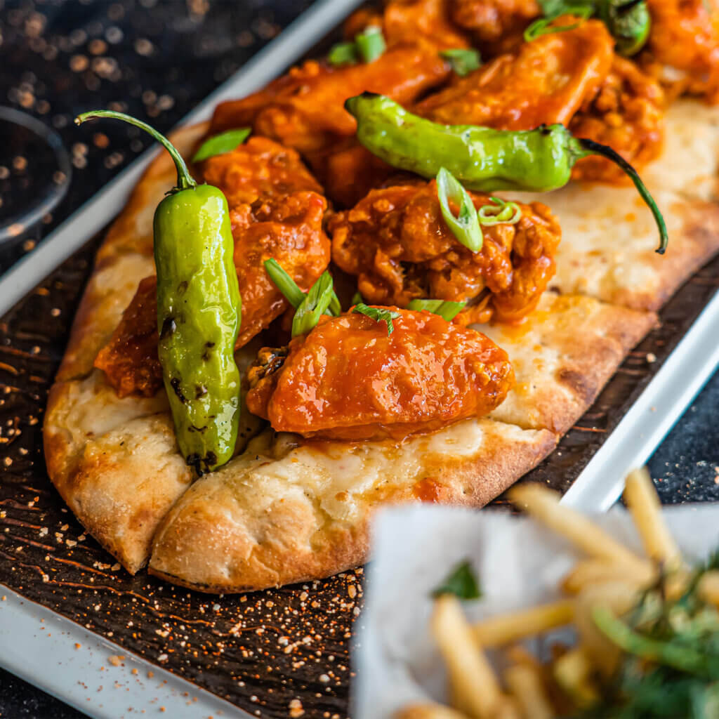A flatbread pizza with buffalo chicken and pickled hot peppers sits on a gourmet plate.