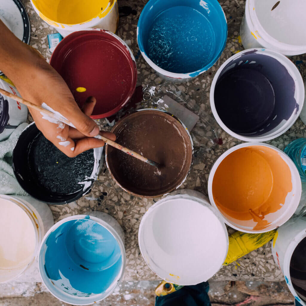 A hand holding a paintbrush reaches in to a paint cup of brown paint, with other paint cups of more paint colours surrounding it, to paint their own pottery, an excellent activity for things to do in Canmore year-round.