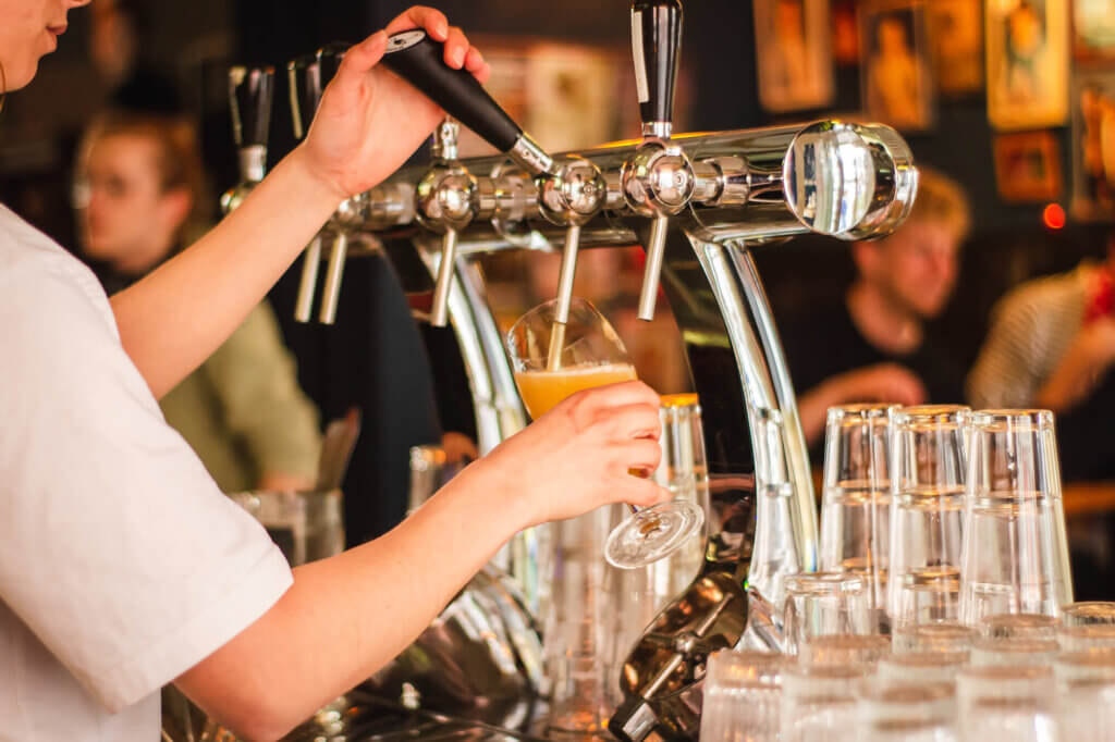 A bar worker pours a glass of beer from a tap at a bar.