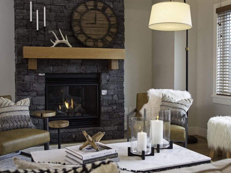 A cozy living room with a stone fireplace, neutral toned colouring and wooden accents in a luxury Tamarack Lodge condo.