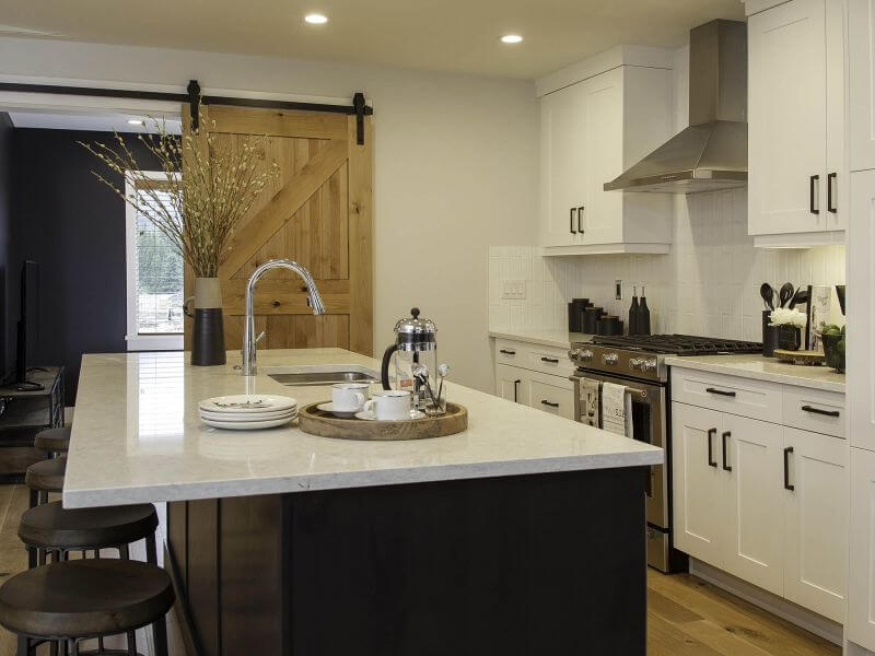 A large and open gourmet kitchen, with white tiles and cabinets, a wooden barn door, hardwood floors, modern appliances and accents, and luxury touches in a Tamarack Lodge condo in Canmore.