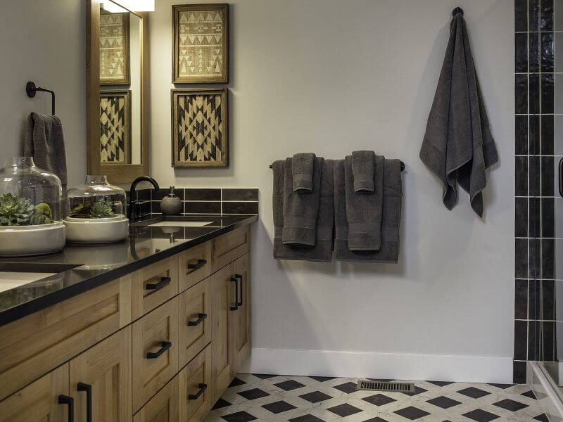 A luxurious, spa llike bathroom with checkered black and marble tiles, dark granite countertops, neutral tones and wooden accents in a Tamarack Lodge luxury condo in Canmore.