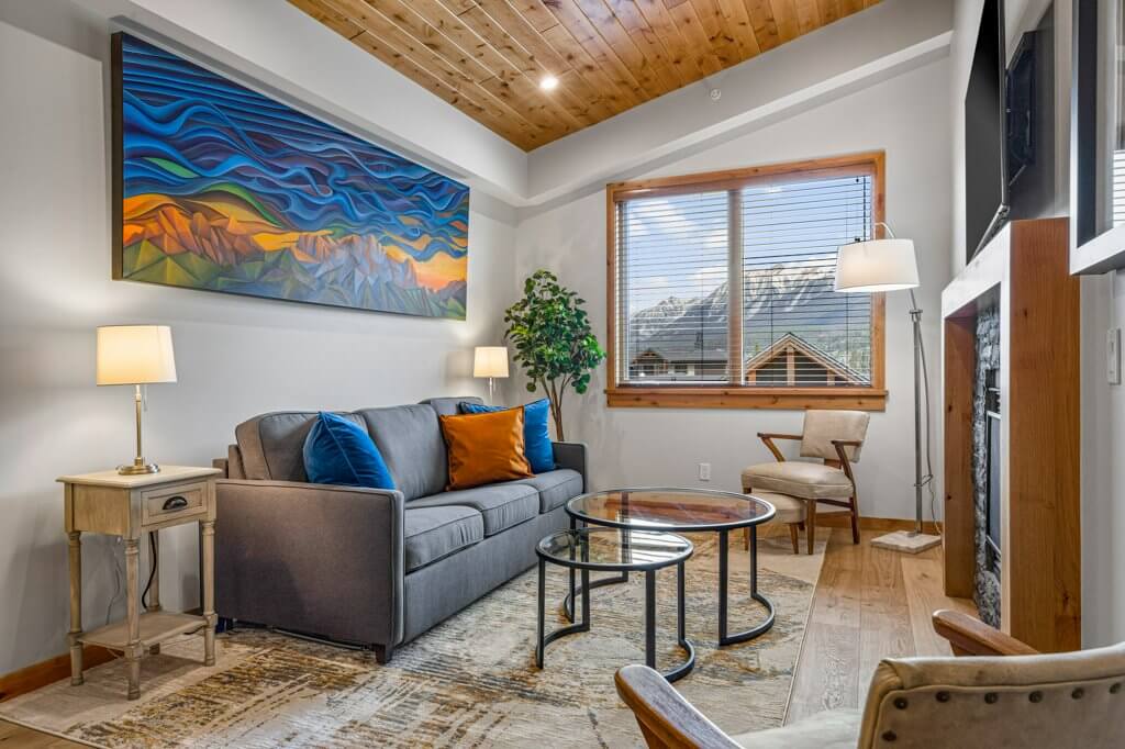 Tamarack Unit 403A's living room with a comfortable grey couch, bright natural light, hardwood floors, and modern finishes located at Spring Creek Vacations in Canmore, Alberta.