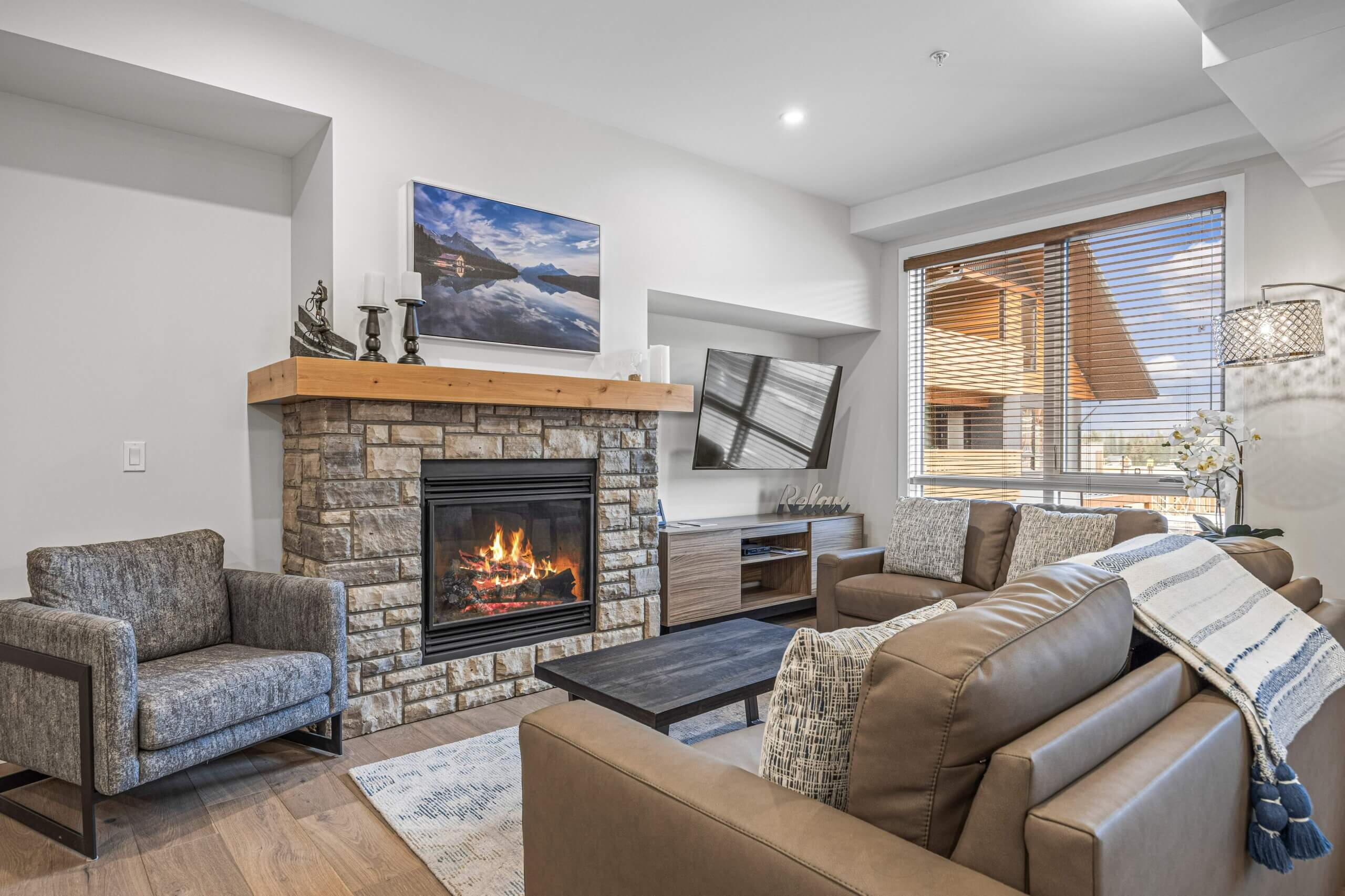 A living room with a cozy stone fireplace and comfortable couch with modern finishes in a Spring Creek Vacations vacation rental in Canmore, Alberta.