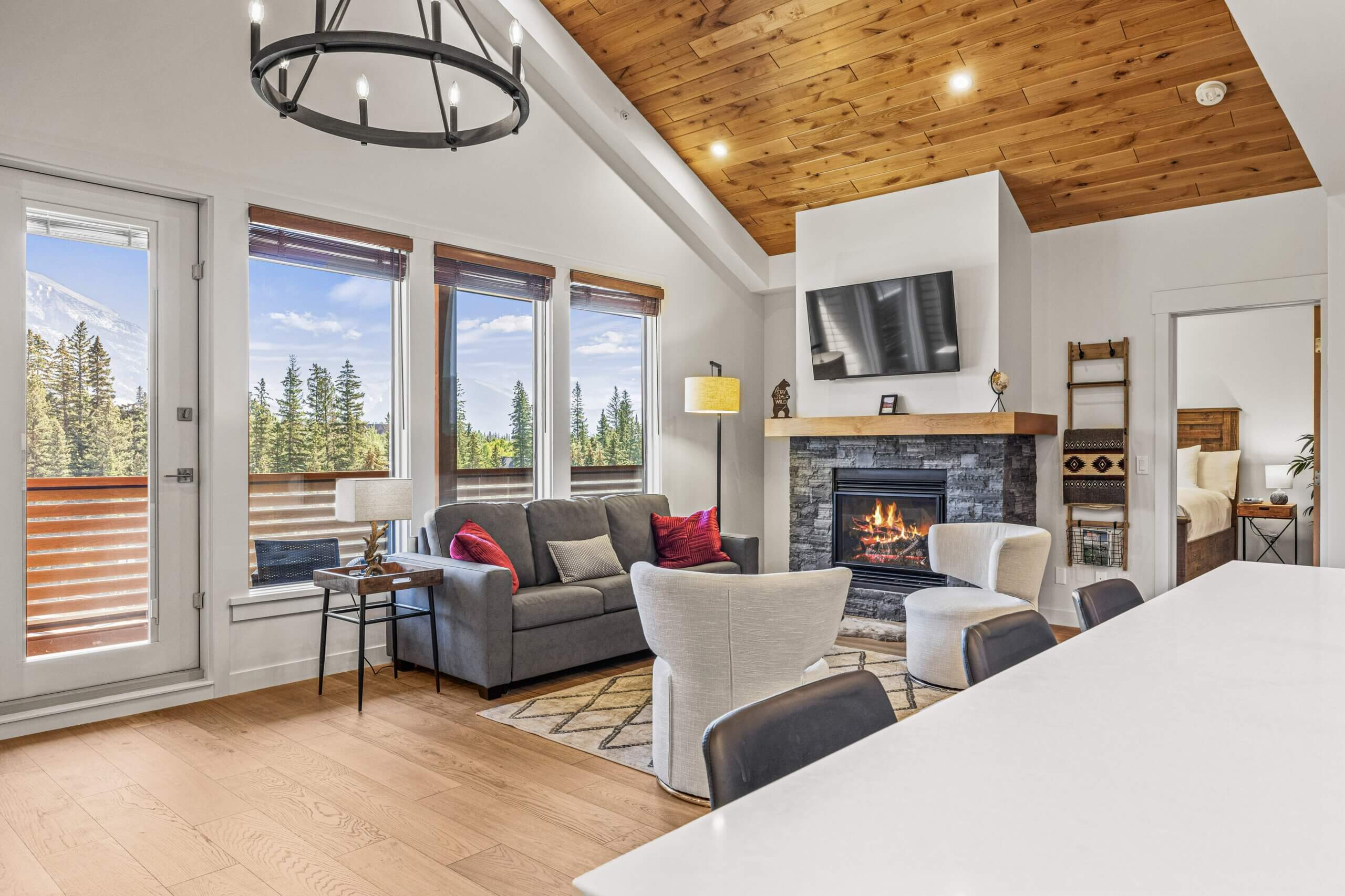 An open concept living room with a comfortable couch, hardwood floors, large bright windows and cozy fireplace in a Spring Creek Vacations' vacation rental in Canmore Alberta.