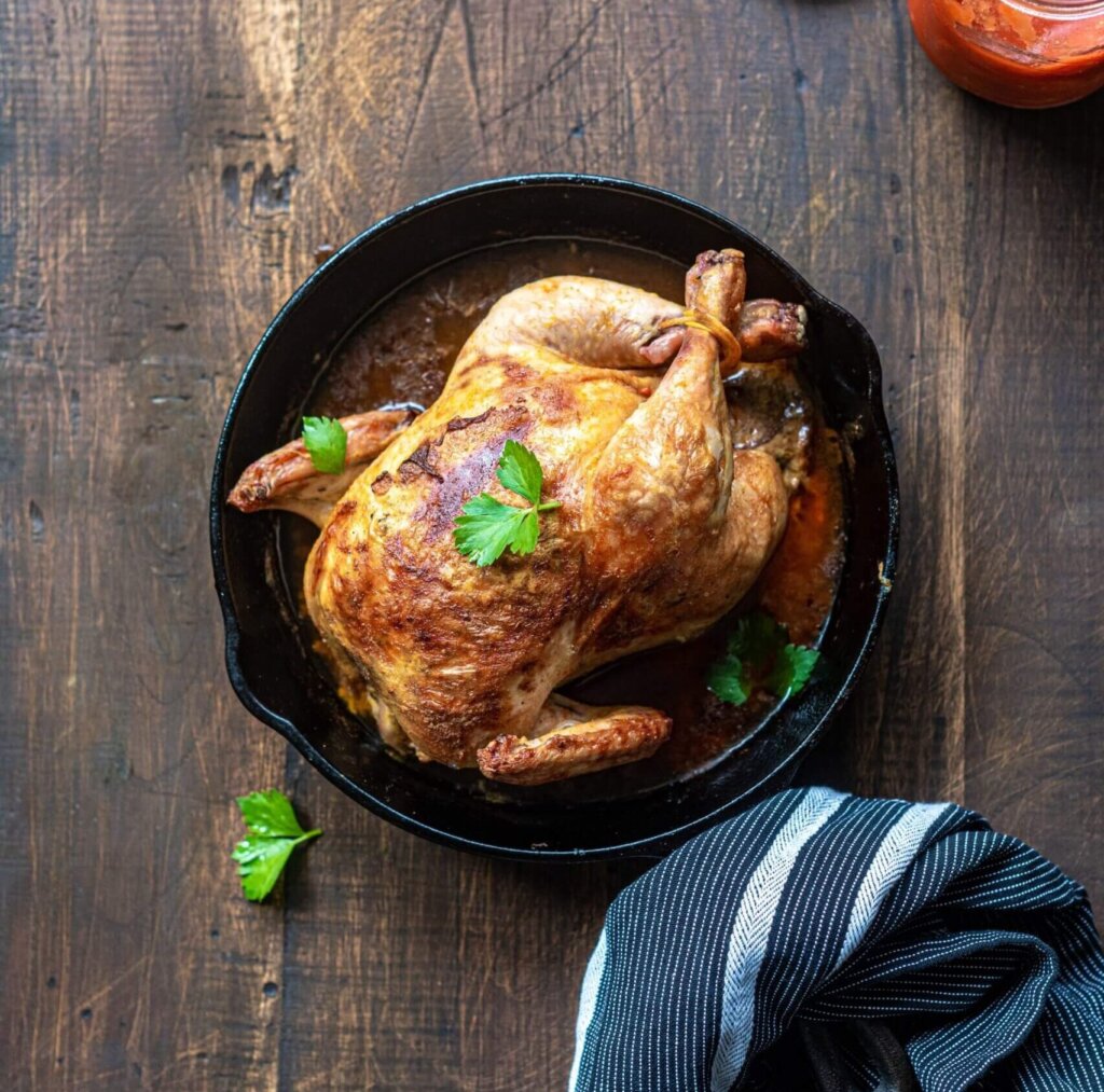 A roast chicken in a cast iron pan on a wooden table, with sauce to the side, cooked on a family vacation in Canmore.