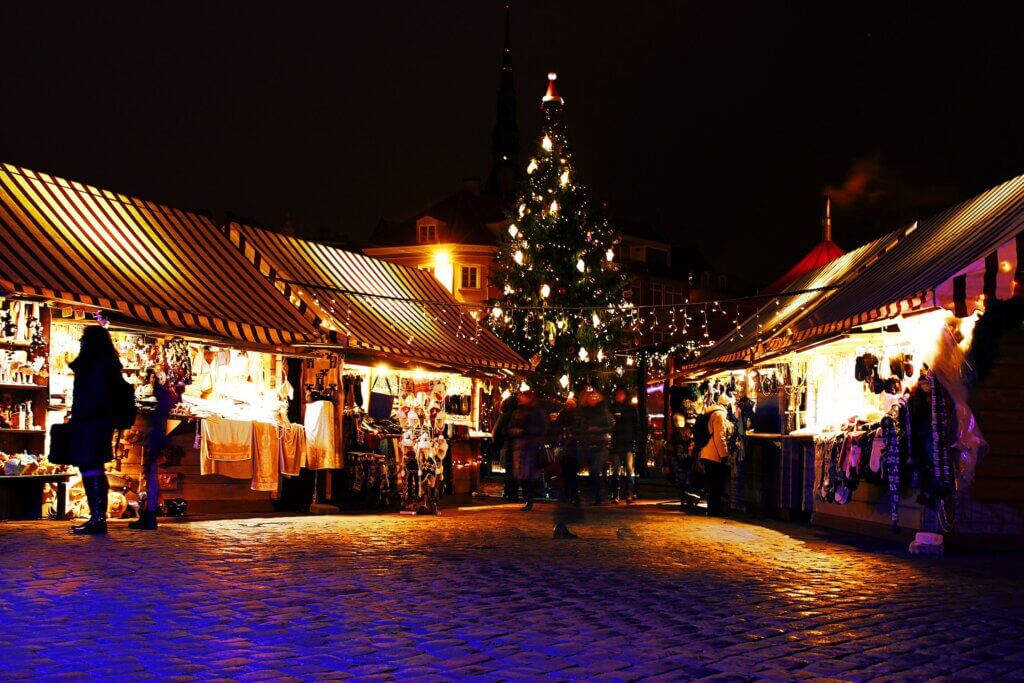 An outdoor Christmas market at night with a light up Christmas tree, artisan stalls and cobbled roads.