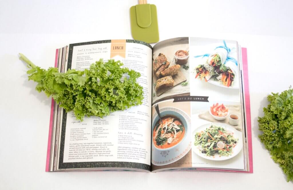 An open recipe book with a lettuce leaf on its pages, on top of a white counter, perfect for helping you cook a family meal while on a family vacation in Canmore.