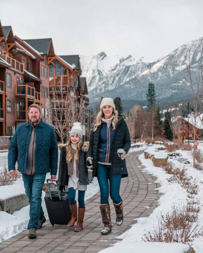A father and mother walk along a brick pathway on a snowy day in Spring Creek, Canmore. Going for a winter walk is a great activity for a family Christmas Vacation.