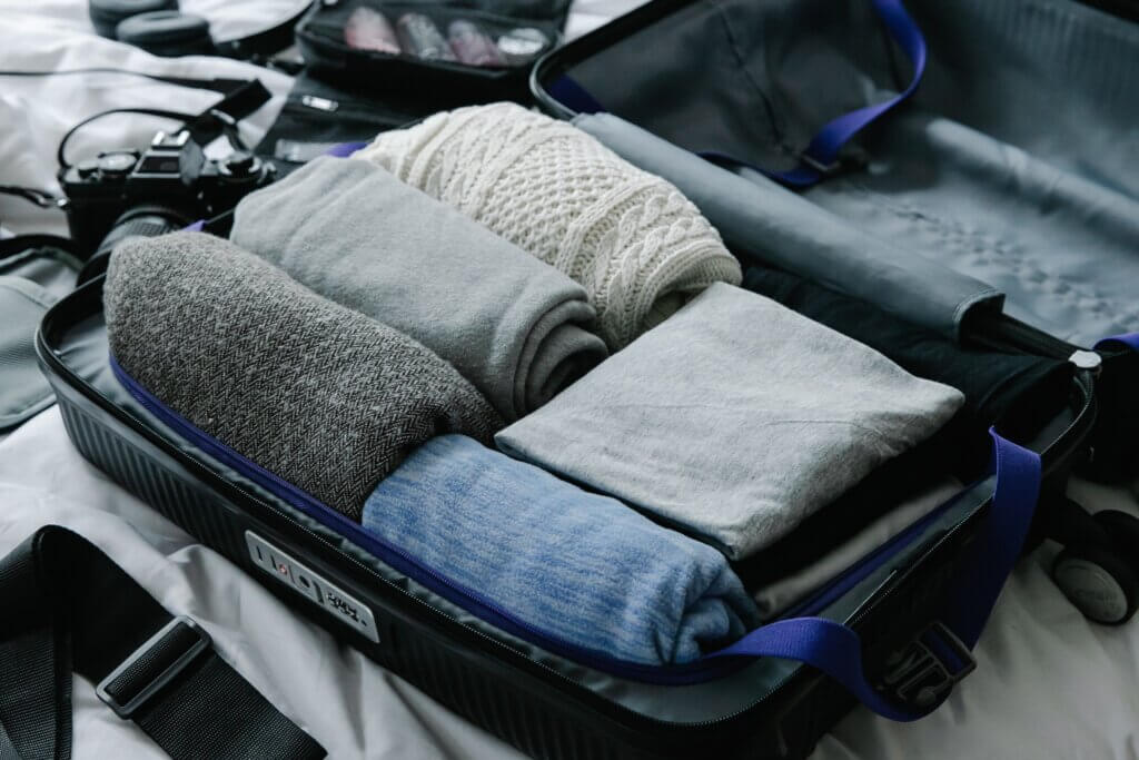 A packed suitcase on a bed with sweaters and clothing inside.