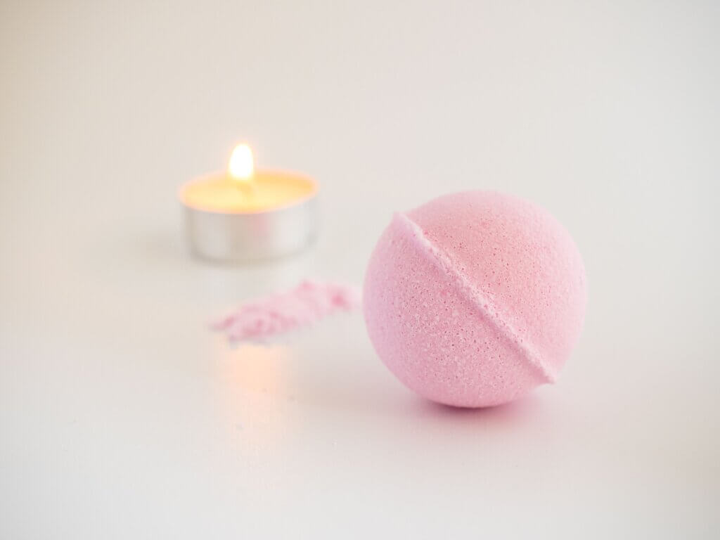 A pink bath bomb on a white surface with a lit tealight candle in the background, perfect for a cozy night in while on a winter trip to Canmore with Spring Creek Vacations.